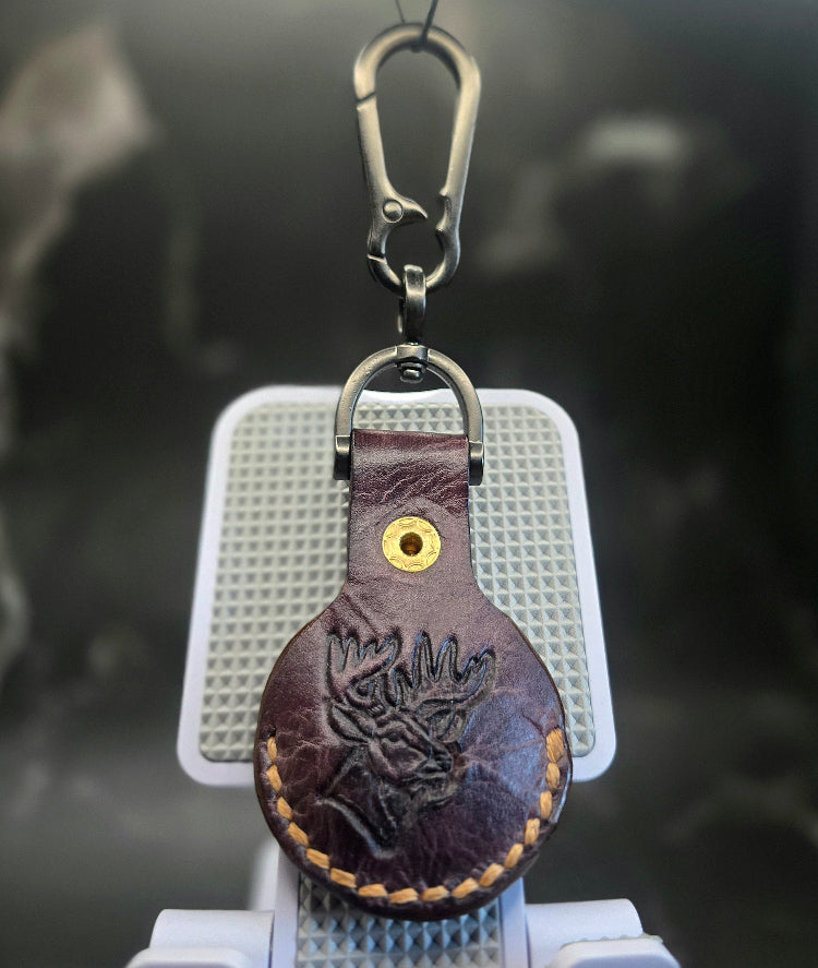 Brown veg-tanned leather apple air tag case with a picture of a deer stamped into it hanging on a solid stainless steel lobster clasp keychain.