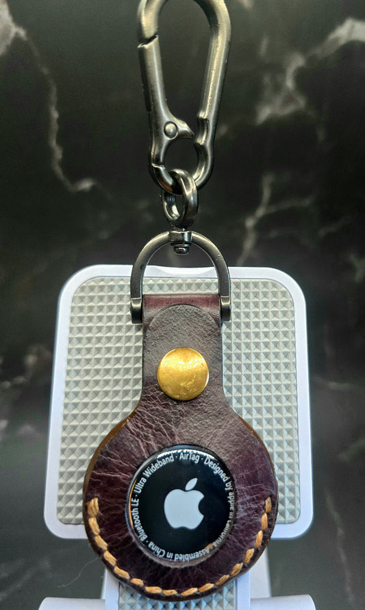 Brown vegetable tanned leather Apple air tag case hanging from a stainless steel keychain with an apple air tag inserted into the case.