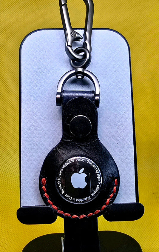 Black premium vegetable tanned leather Apple airtag pouch with red stitching on a stainless steel carabiner.