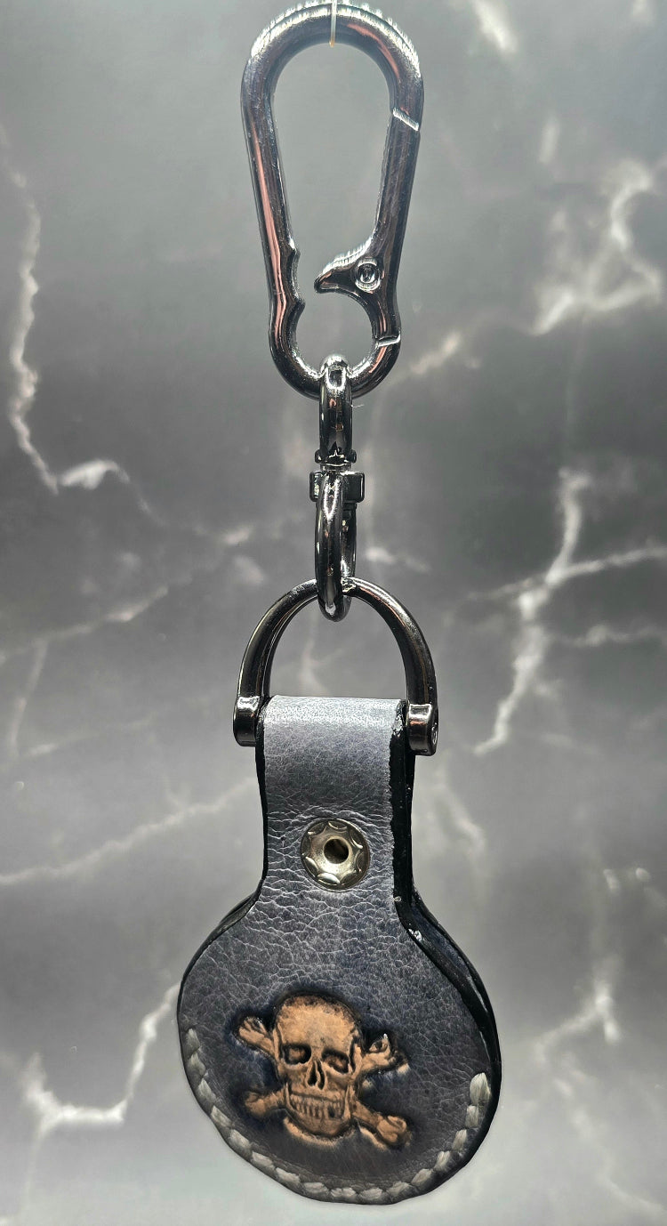 Black veg-tanned leather apple air tag case with a skull and crossbones stamped into it hanging on a solid stainless steel lobster clasp keychain.