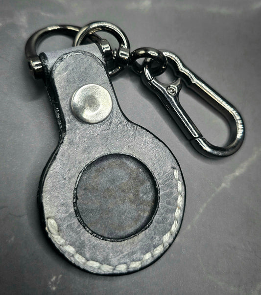 Black vegetable tanned leather Apple air tag case on a stainless steel keychain.