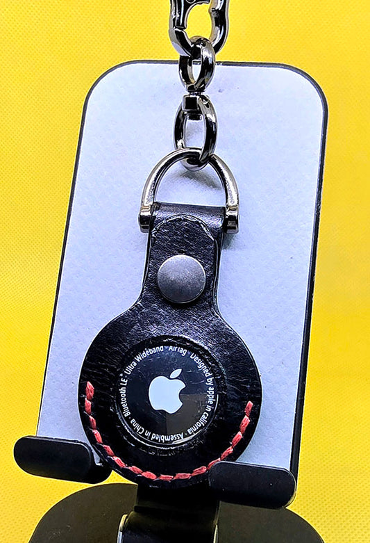 Black apple air tag case with red stitching with air tag inserted on a keychain.