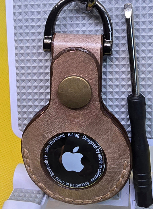 Brown or tan colored apple air tag holder made out of veg-tan leather on a keychain with mini screwdriver next to it.