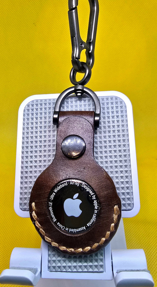 Brown colored apple airtag case on a stainless steel keychain with airtag inserted.