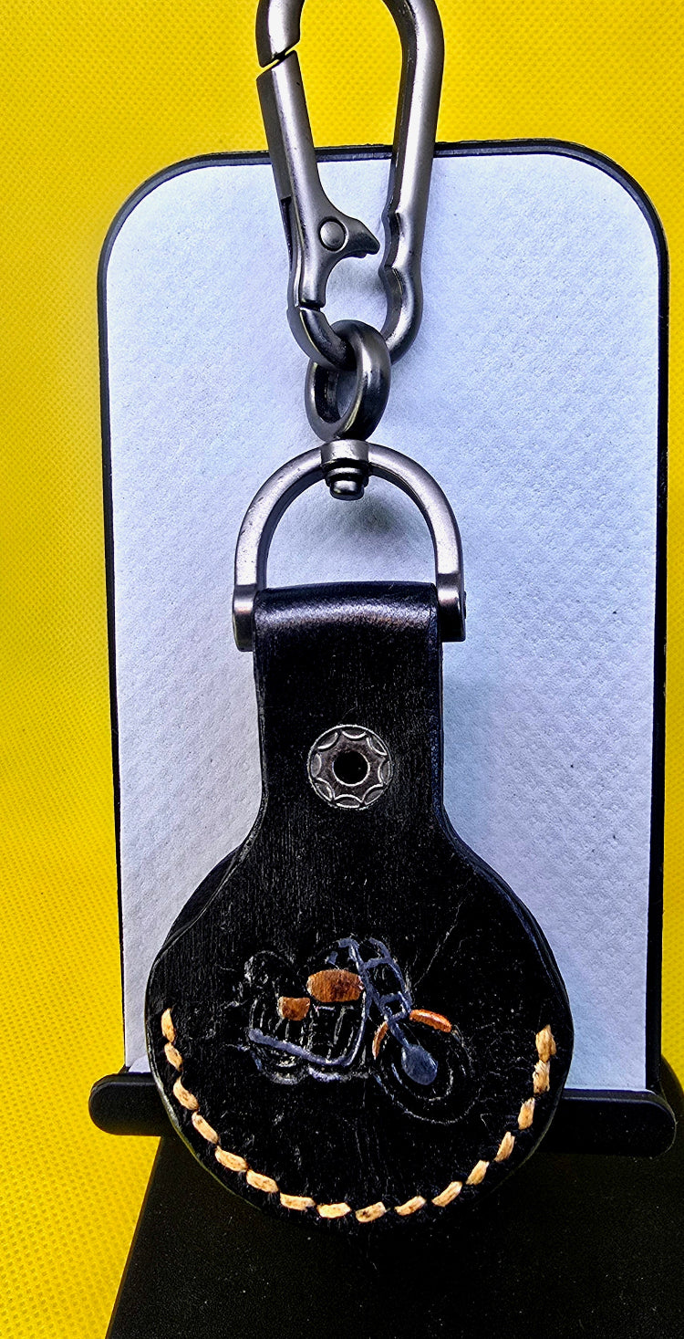 Black vegetable tanned leather apple air tag case with orange stitching, a stamped motorcycle hand-painted orange and black on a solid stainless steel keychain.
