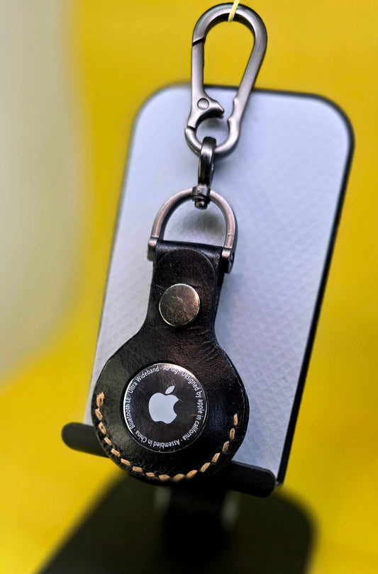 Black vegetable tanned leather apple air tag case with orange stitching on a keychain and containing an apple airtag.