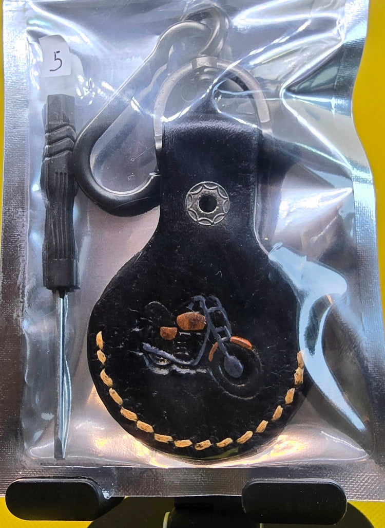 Black vegetable tanned leather apple air tag case with orange stitching, a stamped motorcycle hand-painted orange and black on a solid stainless steel keychain.