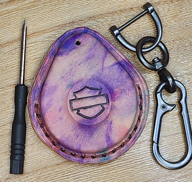 Front view of a premium vegetable tanned leather Harley Davidson key fob case with a unique tye dye look of purple with splashes of pink and green. Solid stainless steel lobster clasp style keychain and mini screwdriver included in photo on each side.