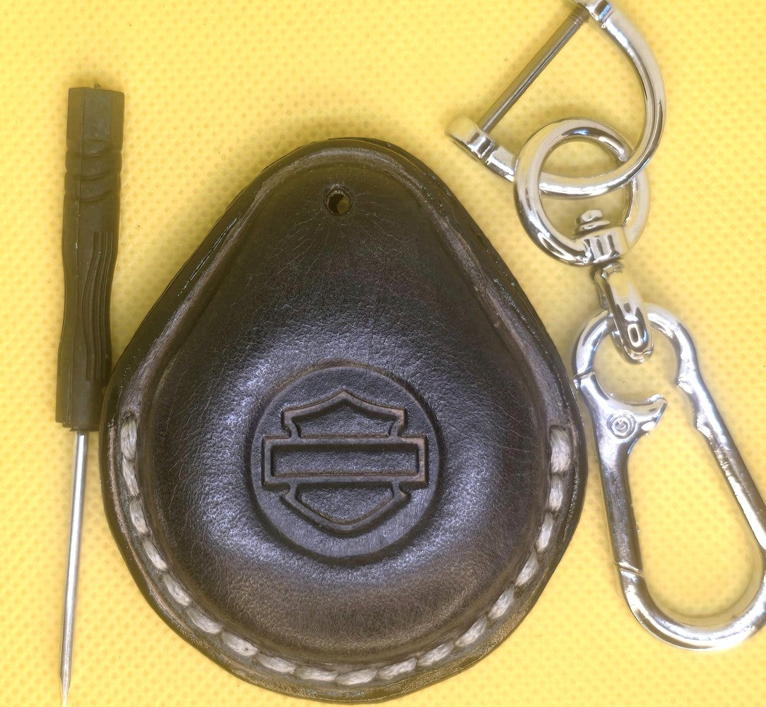Picture of a charcoal gray colored vegetable tanned leather key fob case for Harley Davidson motorcycles with light gray stitching on a table with the included stainless steel keychain and screwdriver.