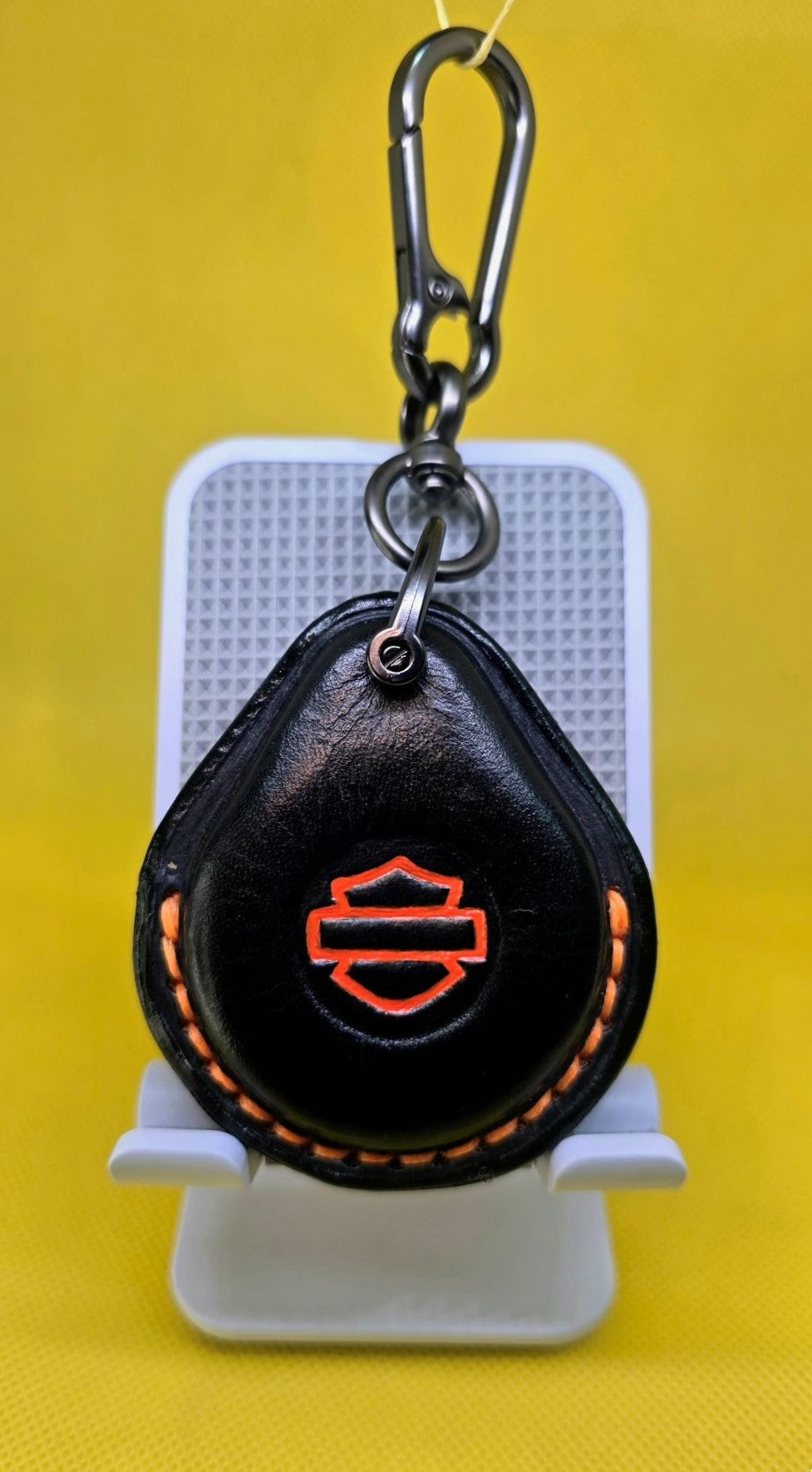 Black vegetable tanned leather key fob case for Harley Davidson motorcycles with orange stitching and logo hanging on a lobster clasp keychain.