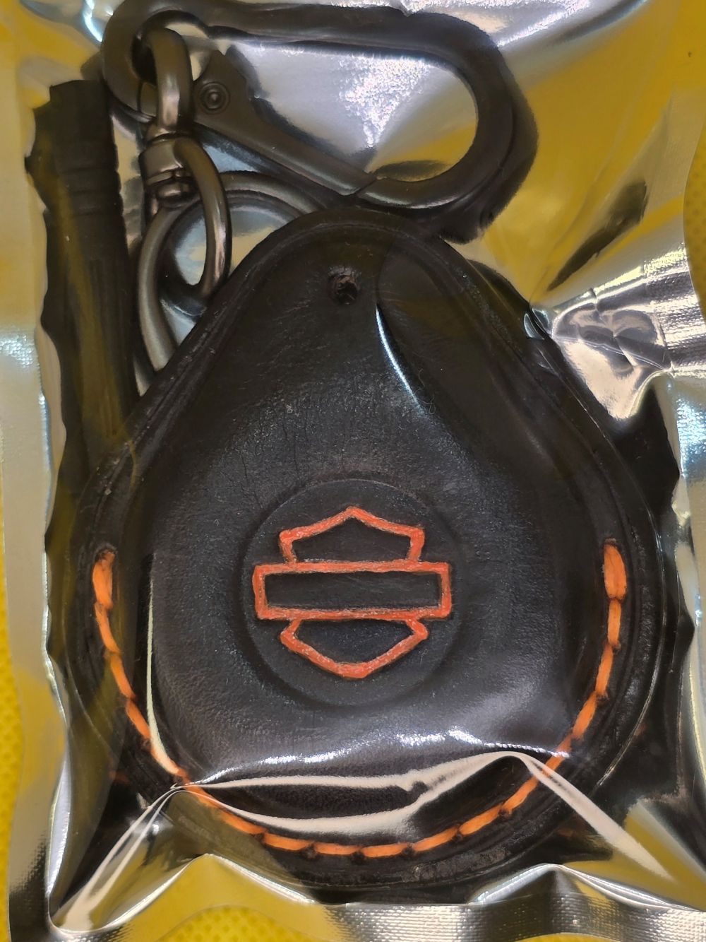 Black and orange veg-tan leather key fob case for Harley Davidson motorcycles with orange logo and stitching in retail packaging with included stainless steel lobster clasp keychain and mini screwdriver.