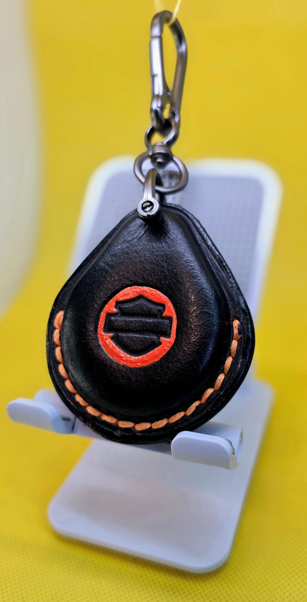 Black vegetable tanned leather key fob case for Harley Davidson motorcycles with orange stitching and logo hanging on a lobster clasp keychain.