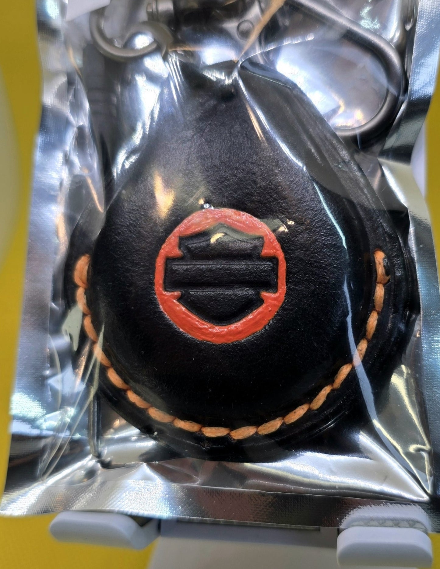 Black and veg-tan leather key fob case for Harley Davidson motorcycles with orange logo and stitching in retail packaging with included stainless steel lobster clasp keychain and mini screwdriver.