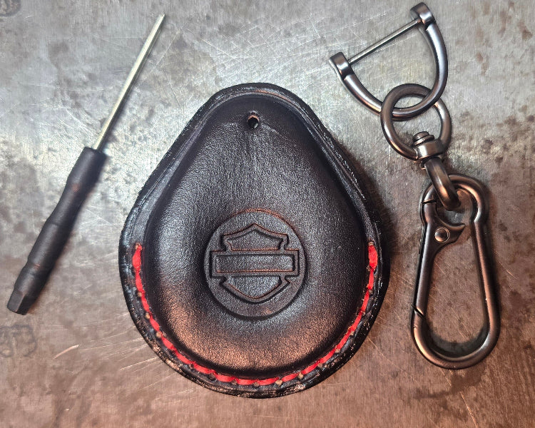 Picture of a black vegetable tanned leather key fob case for Harley Davidson motorcycles with red stitching with the included stainless steel keychain and screwdriver.
