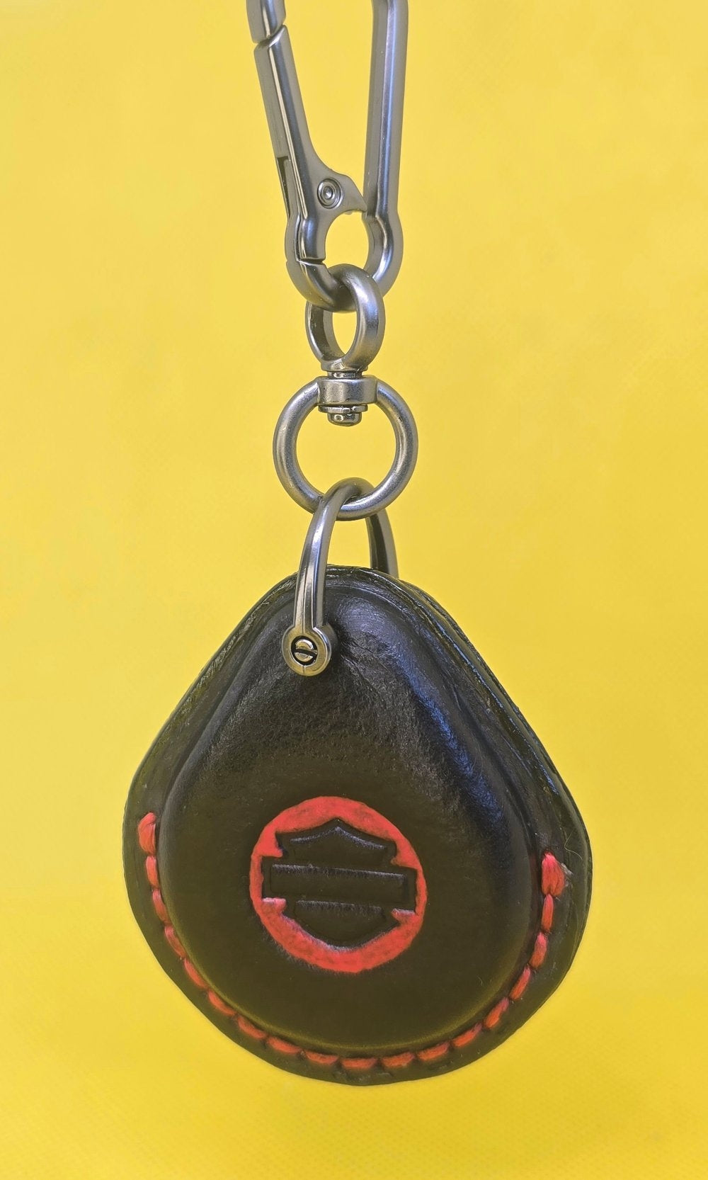 Black and red veg-tan leather key fob case for Harley Davidson motorcycles with red stitching hanging on a lobster clasp keychain.