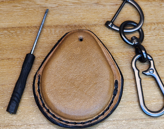 Back view of a light brown vegetable tanned leather key-fob case with black stitching for Harley Davidson motorcycles with a keychain and screwdriver.