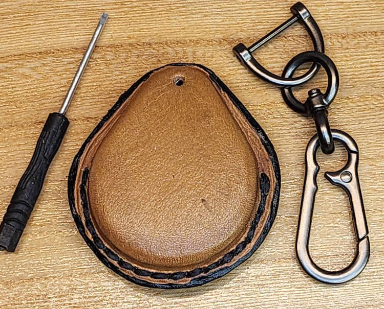Back view of a light brown vegetable tanned leather key fob cases for Harley Davidson motorcycles with black stitching beside the included solid stainless steel lobster clasp keychain and small screwdriver.