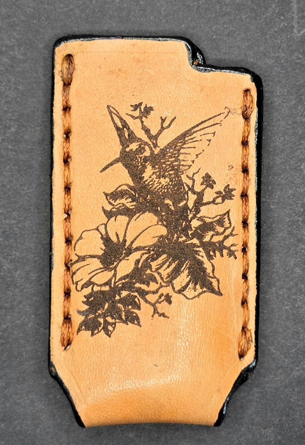 Light brown veg-tan leather Bic lighter case with a hummingbird laser engraved into it.