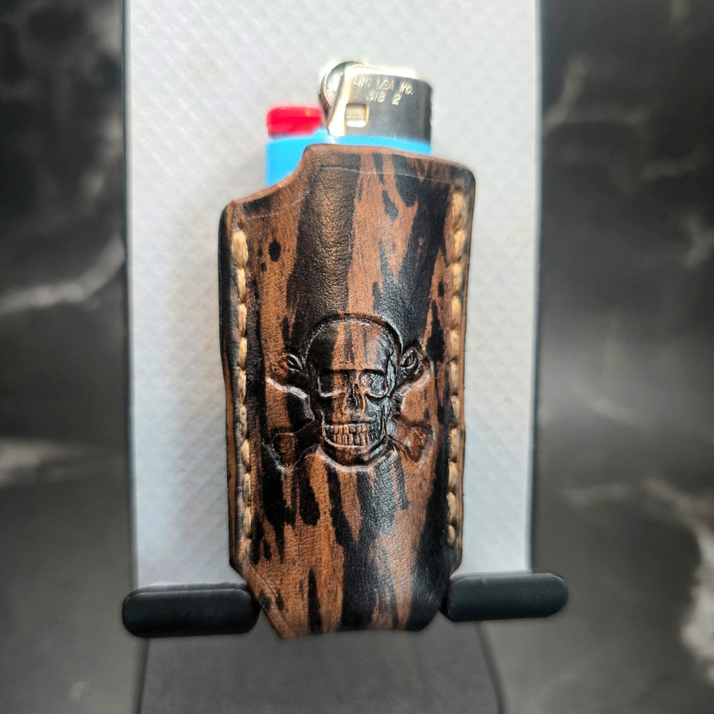 Black and brown camo-style veg-tan leather lighter case for bic lighters with a skull and crossbones stamped into it.