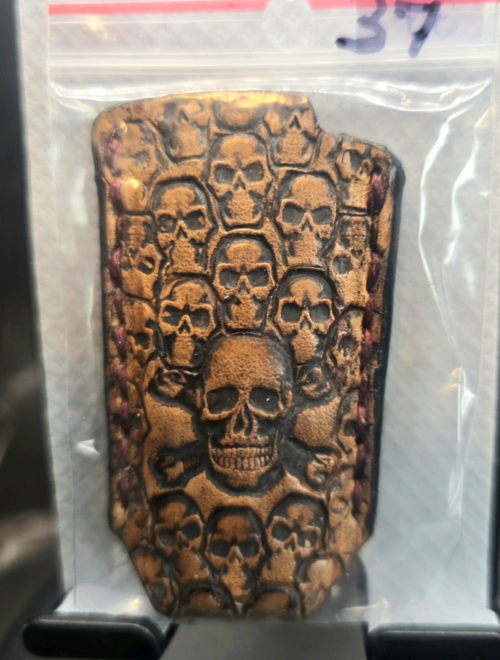 Light brown vegetable tanned leather lighter case for bic lighters with many skulls stamped into it in retail packaging. Crafted in Canada by JnRcreativeCrafts.