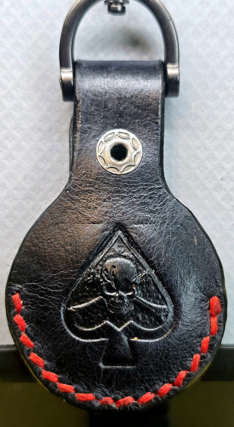 Full-grain veg-tanned leather apple airtag pouch with red stitching and a spade with skull and crossbones stamped into it.