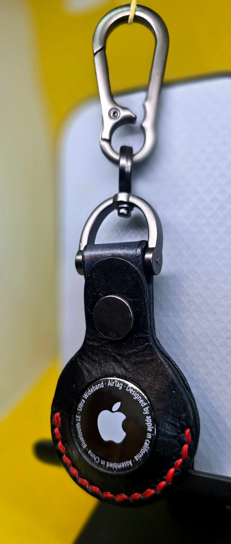 Black premium leather apple air tag case with red stitching on a solid stainless steel lobster clasp keychain.