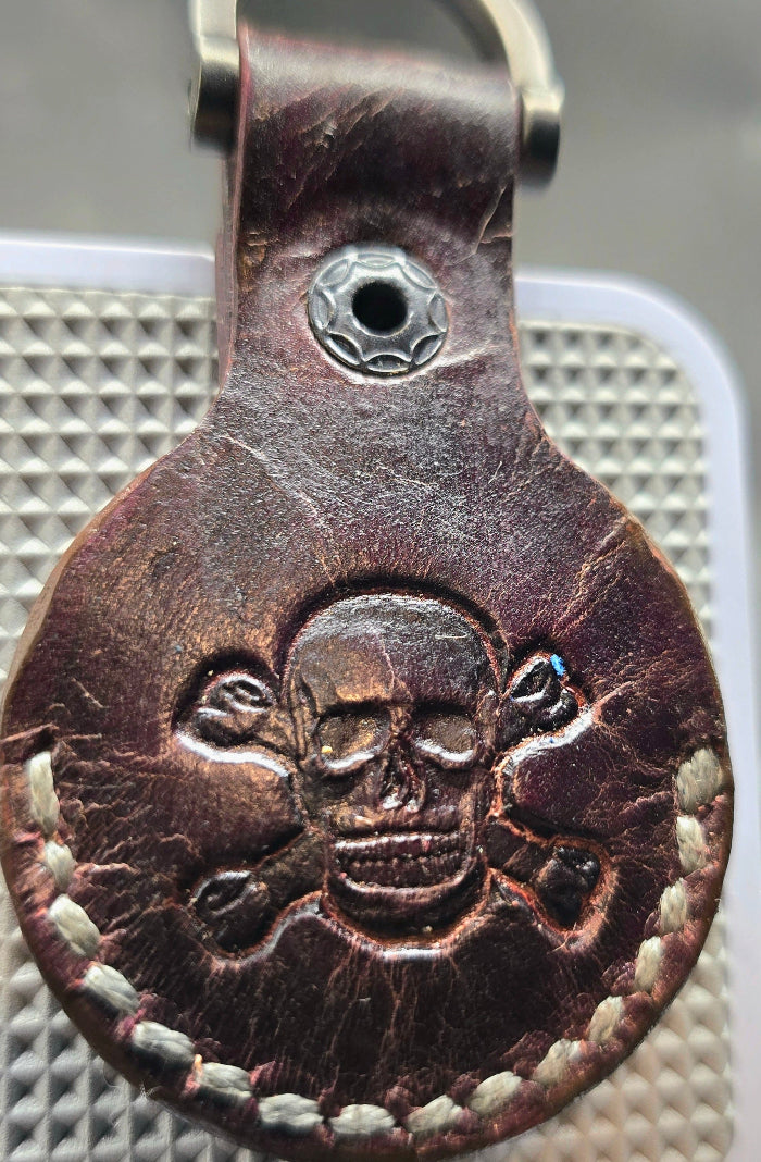 Brown veg-tanned leather apple air tag case with a skull and crossbones stamped into it.