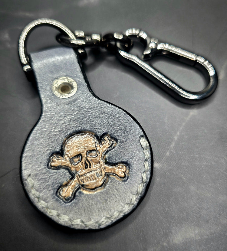 Black veg-tanned leather apple air tag case with a light brown skull and crossbones stamped into it.