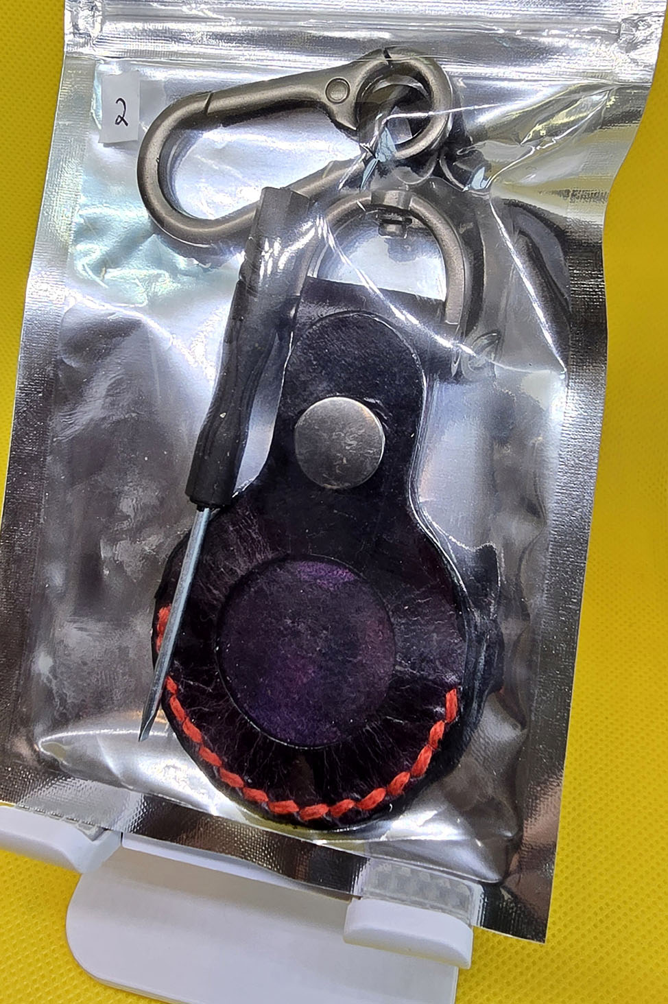 Black apple airtag with red stitching in retail packaging  with keychain included.