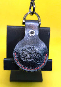 Veg-tanned leather Apple airtag case with a motorcycle stamped into it with red stitching on a solid keychain.