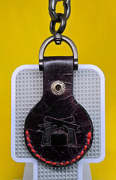 Black vegetable tanned leather apple airtag case with red stitching and 2 hand guns stamped into it.