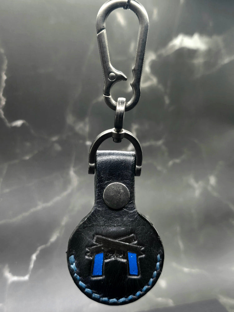Video of a black colored vegetable tanned leather Apple Air tag holder with  2 navy blue guns stamped into it hanging on a lobster clasp keychain.