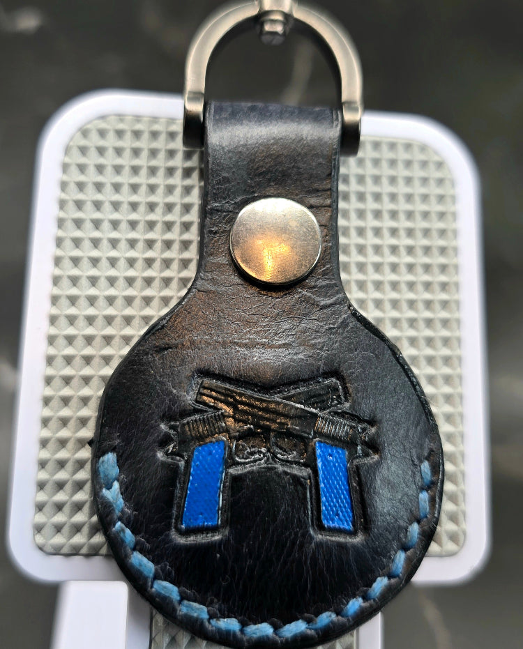 Black veg-tan leather apple air tag case with blue stitching and 2  navy blue guns stamped into it on a keychain.