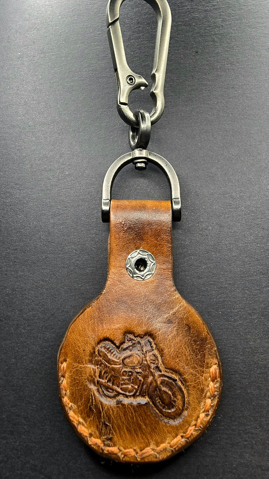 Brown veg-tanned leather apple airtag case with a motorcycle stamped into it on a stainless steel keychain.