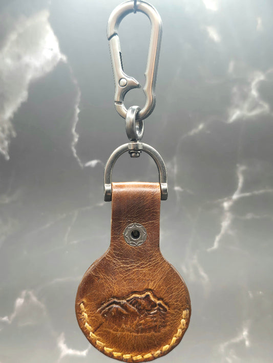 Brown veg-tanned leather apple air tag case with a mountain scene  stamped into it.