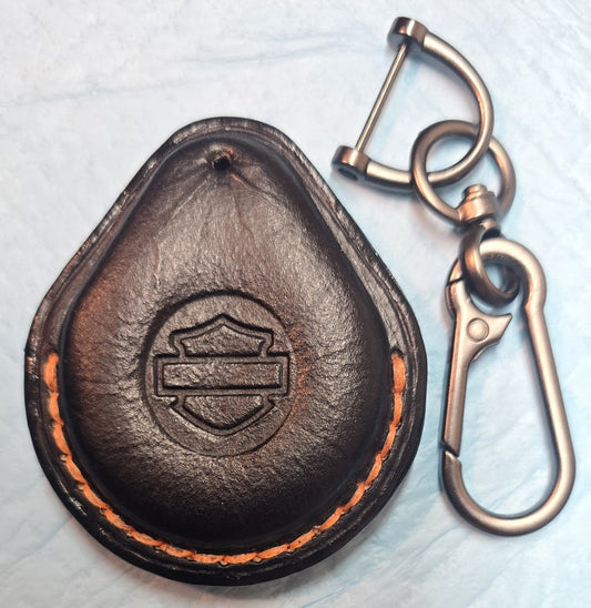 Black veg-tan leather key fob case for Harley Davidson motorcycles with orange stitching next to a stainless steel lobster clasp style keychain.