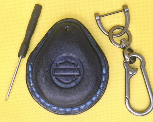 Picture of a navy blue colored  vegetable tanned leather key fob case for Harley Davidson motorcycles with blue stitching on a table with the included stainless steel keychain and screwdriver.