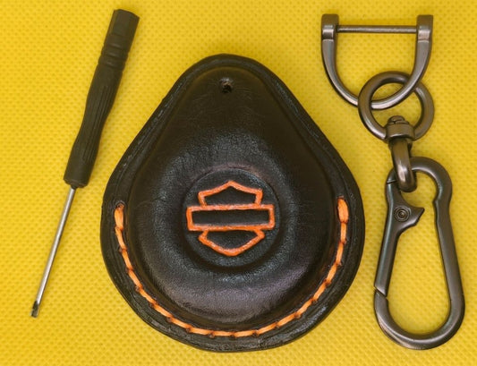 Picture of a black vegetable tanned leather key fob case for Harley Davidson motorcycles with orange stitching on a table with the included stainless steel keychain and screwdriver.