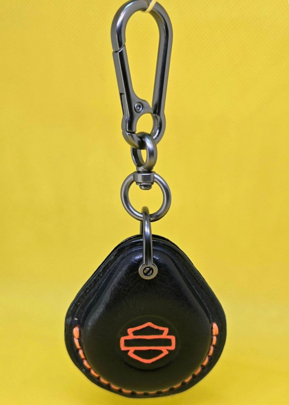 Black veg-tan leather key fob case for Harley Davidson motorcycles with orange stitching and logo hanging on a stainless steel lobster clasp keychain.