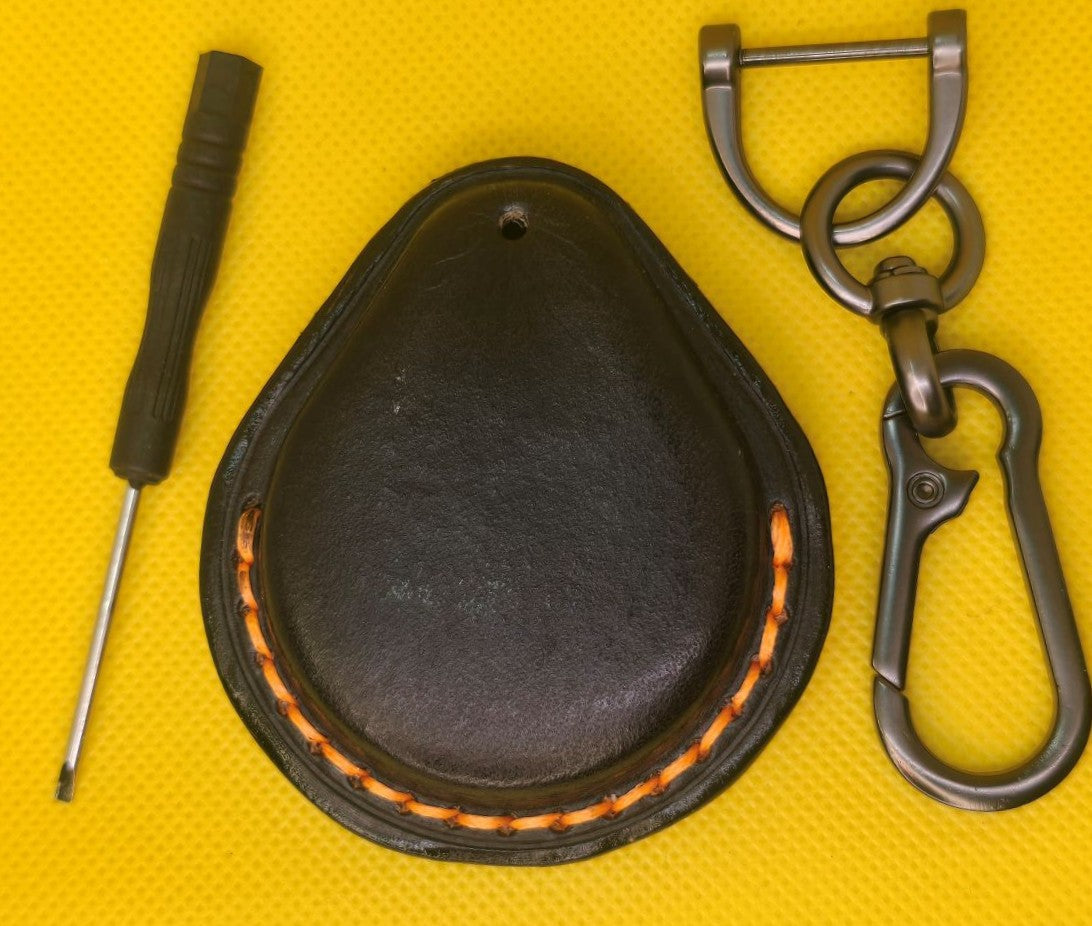 Back view of a black veg-tan leather key fob case for Harley Davidson motorcycles with orange stitching on a table with a lobster clasp keychain and the included mini  screwdriver.