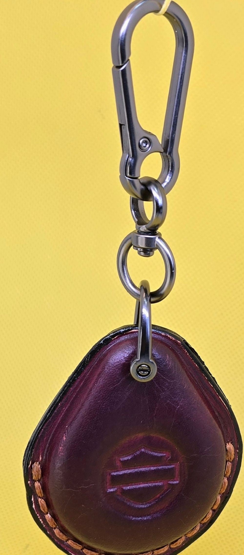 Burgundy veg-tan leather key fob case for Harley Davidson motorcycles with orange stitching and logo hanging on a stainless steel lobster clasp keychain.