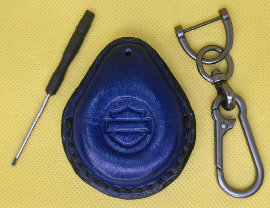 Picture of a navy blue colored  vegetable tanned leather key fob case for Harley Davidson motorcycles with black stitching on a table with the included stainless steel keychain and screwdriver.