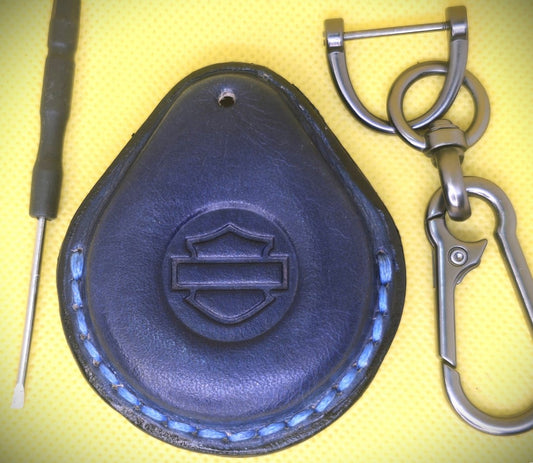 Picture of a navy blue colored  vegetable tanned leather key fob case for Harley Davidson motorcycles with blue stitching on a table with the included stainless steel keychain and screwdriver.