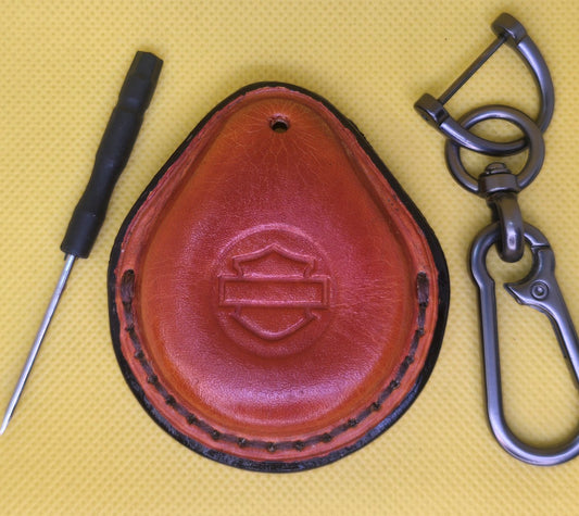 Picture of an orange vegetable tanned leather key fob case for Harley Davidson motorcycles on a table with the included stainless steel keychain and screwdriver.