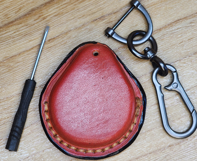 Back view of a Orange colored Vegetable tanned leather key fob case for Harley Davidson motorcycles with a keychain and a screwdriver next to it.