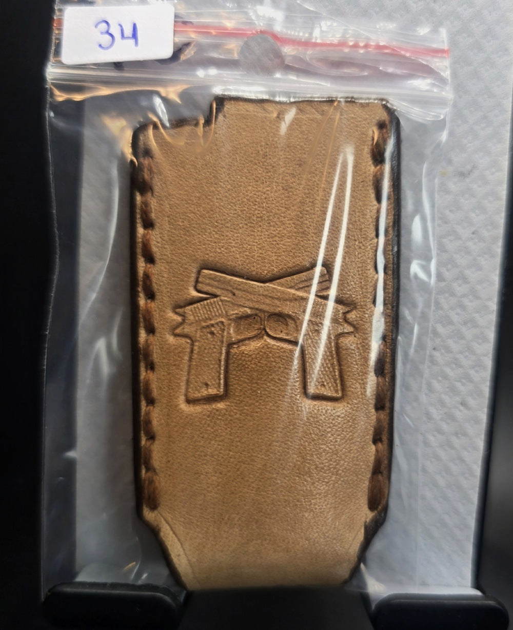 Light brown veg-tan leather Bic lighter case with a pair of handguns stamped into it in retail packaging.