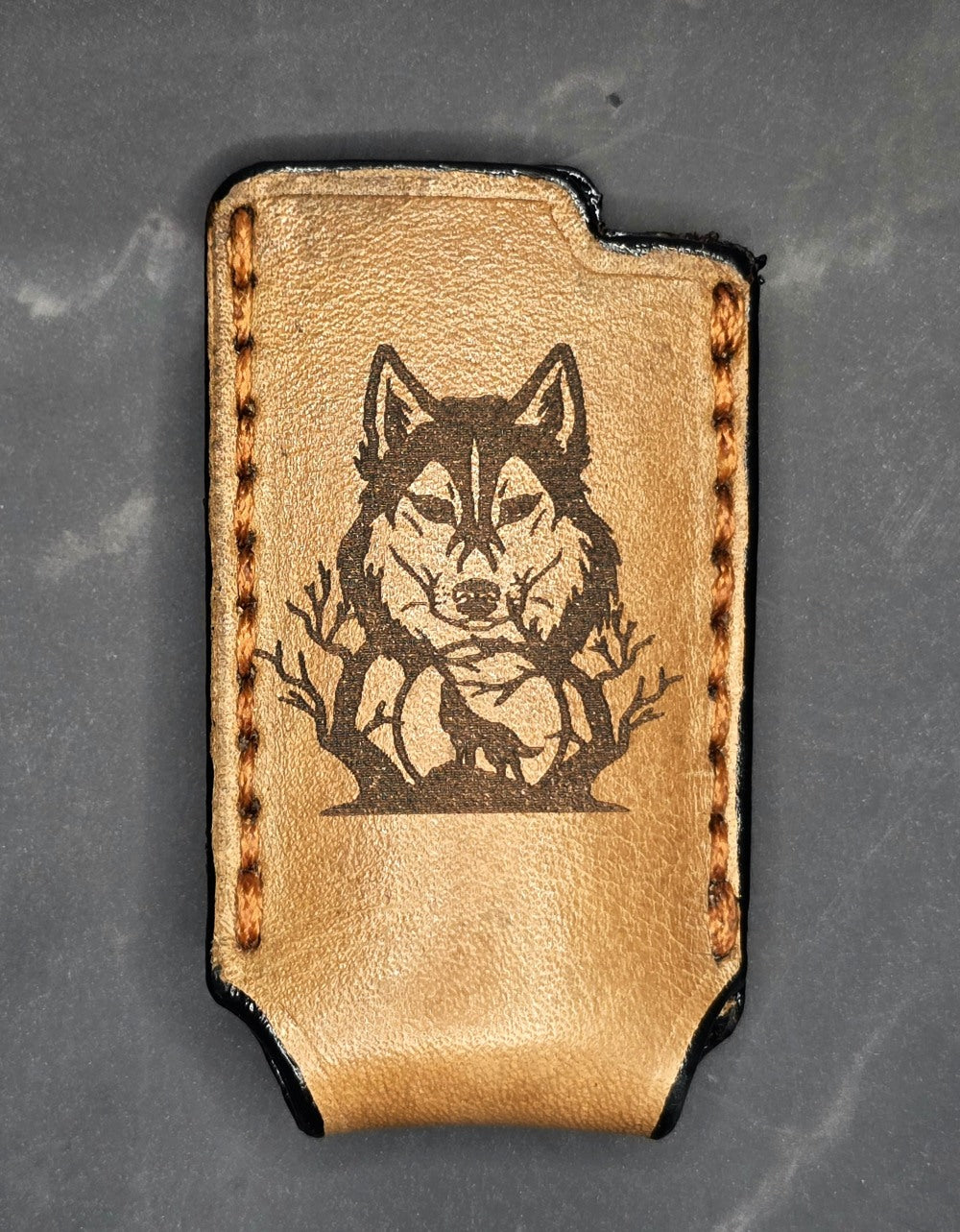 Light brown veg-tanned leather lighter case for bic lighters with a wolf  over a moon laser engraved on it.