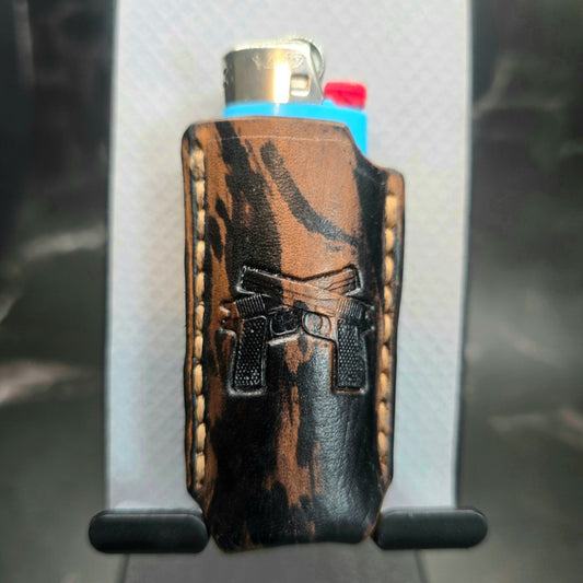 Black and brown camo-style veg-tan leather lighter case for bic lighters with a pair of handguns stamped into it.