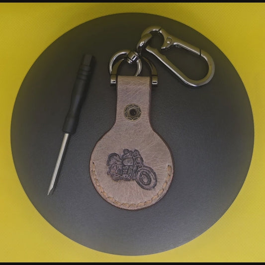 Brown Vegetable tanned leather Apple Airtag holder with motorcycle stamped into it on a keychain clasp turning on a display pedestal.