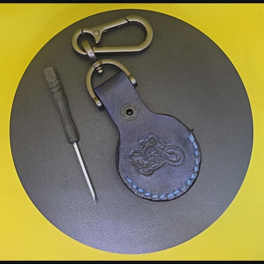 Video of a navy blue vegetable tanned leather Apple Airtag holder with a motorcycle stamped into it on a lobster clasp keychain turning on a display pedestal.